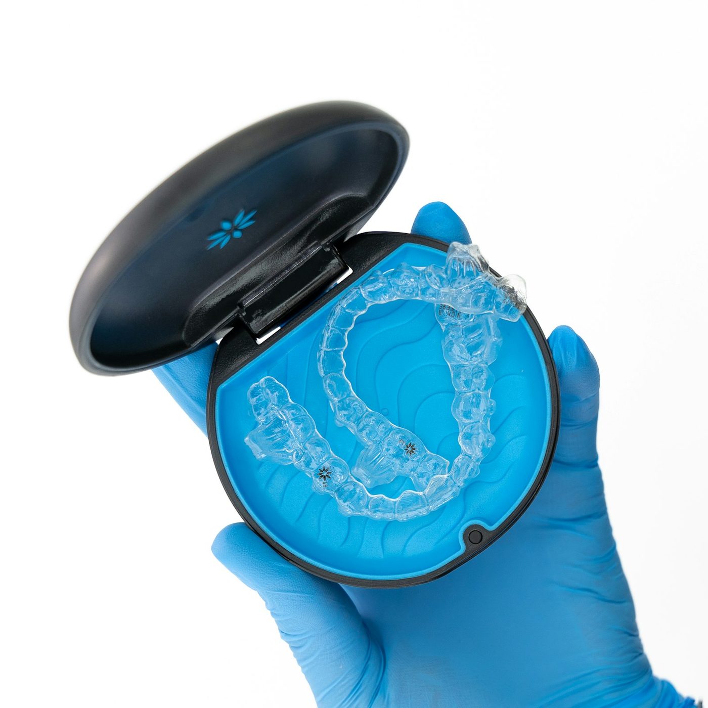 Gloved hand holding an open case with a clear aligner inside